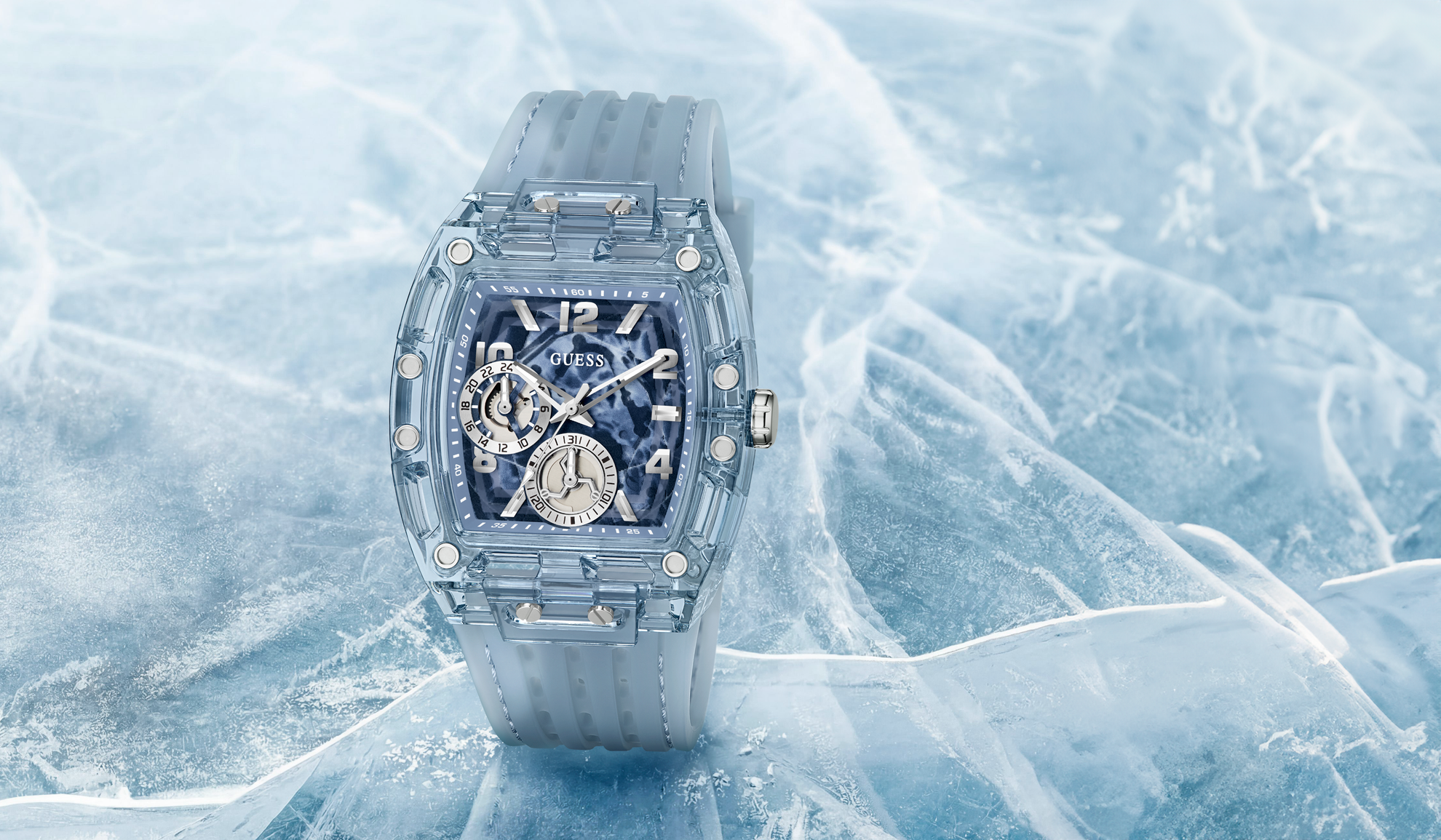 A luxury skeleton watch with a translucent gray resin case and strap, displayed on a bed of textured ice. The watch features a blue-toned skeleton dial with silver-tone hands and markers.