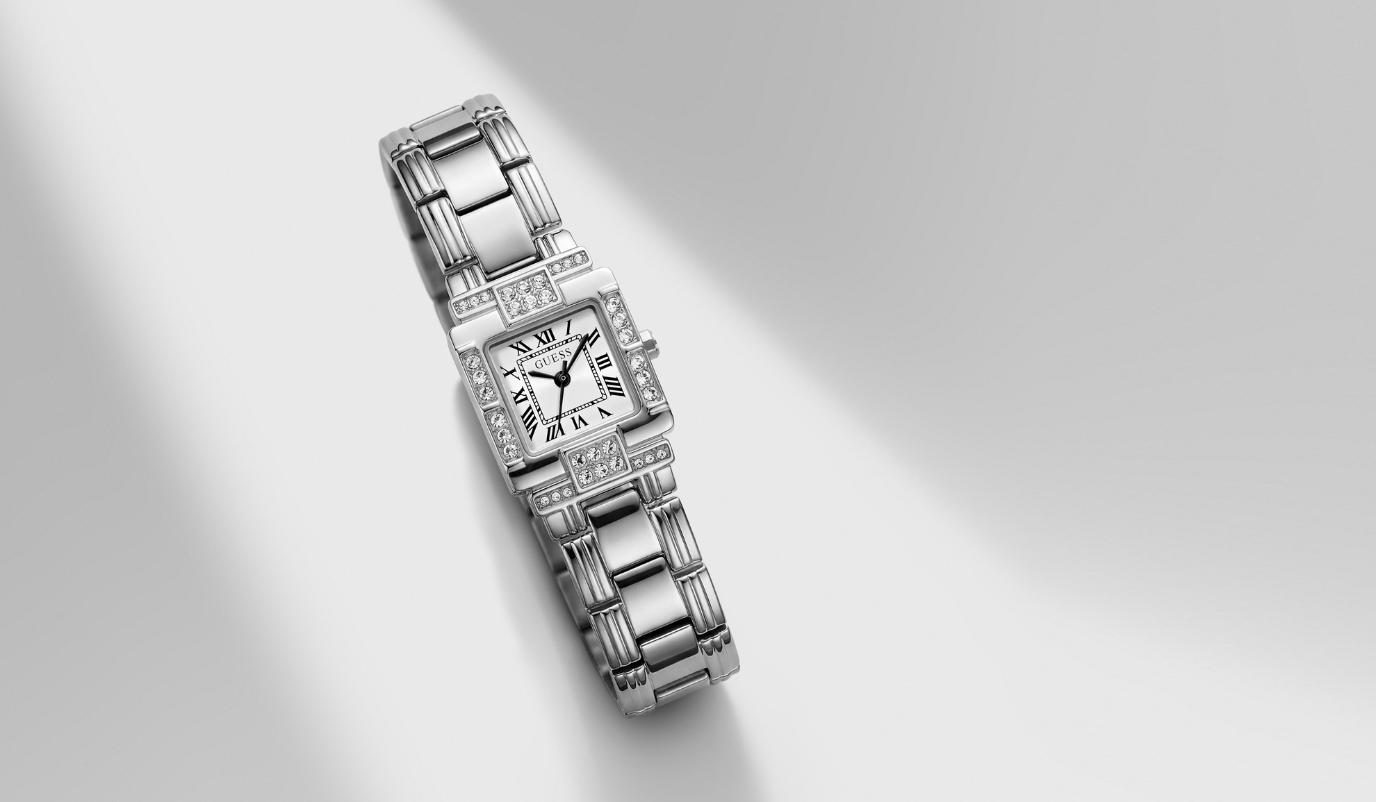 A silver-toned GUESS watch with a diamond-encrusted bezel and matching diamond-set bracelet, displayed diagonally on a light gray background with soft shadows.