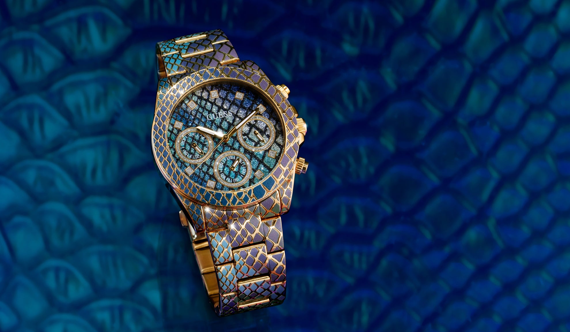 GUESS iridescent python patterned  watch with gemstone accents on a blue textured background