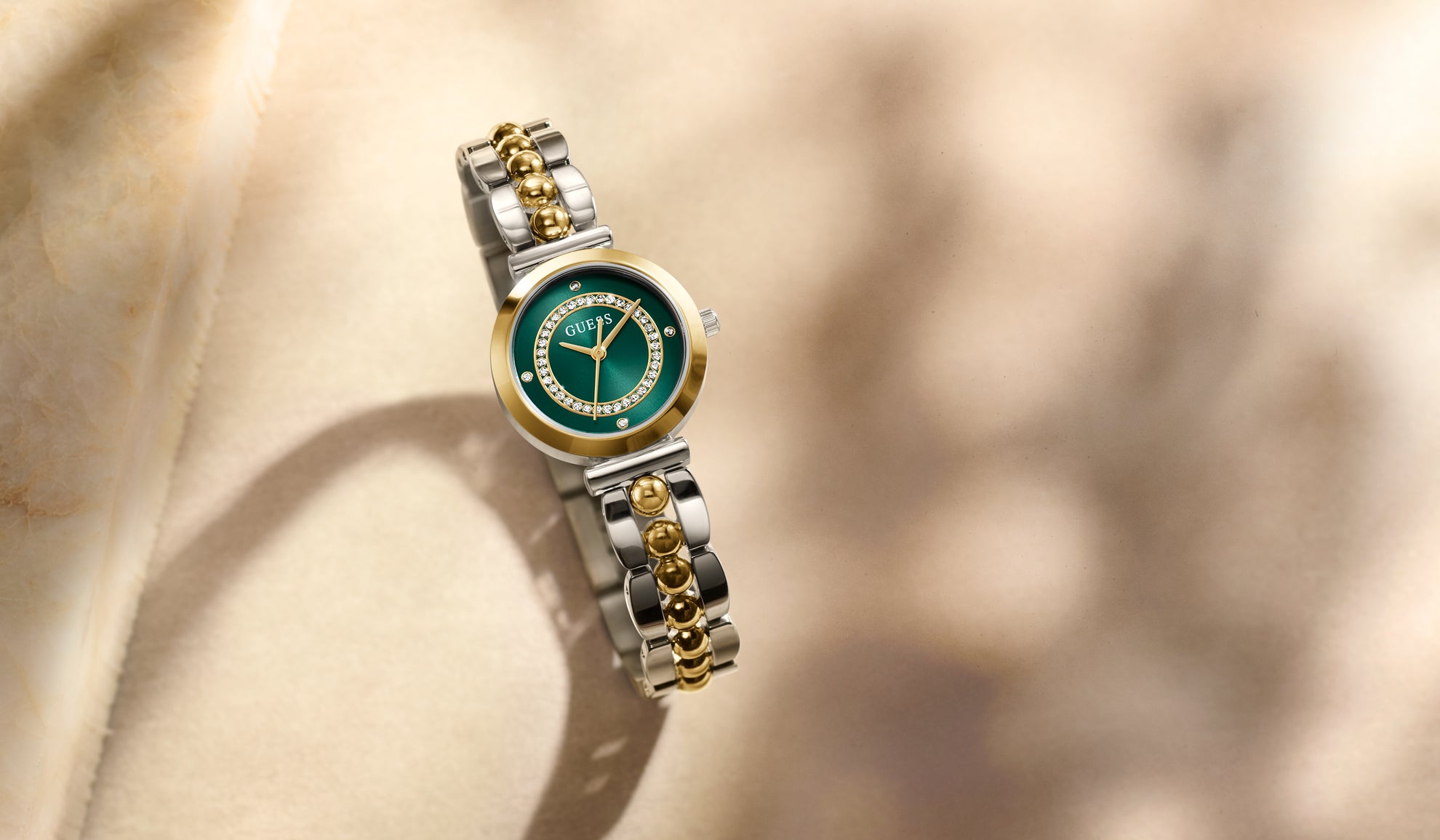 GUESS watch with green face and gold accents on a beige background