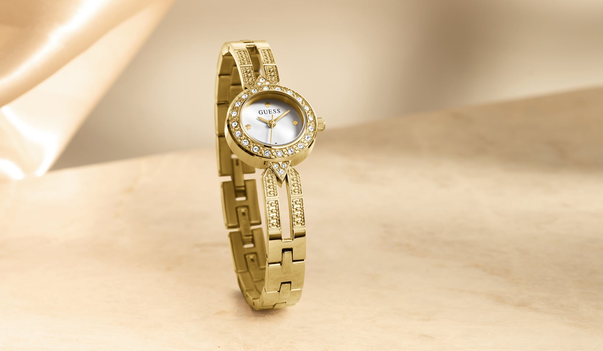 Gold wristwatch with a diamond-studded band on a beige background