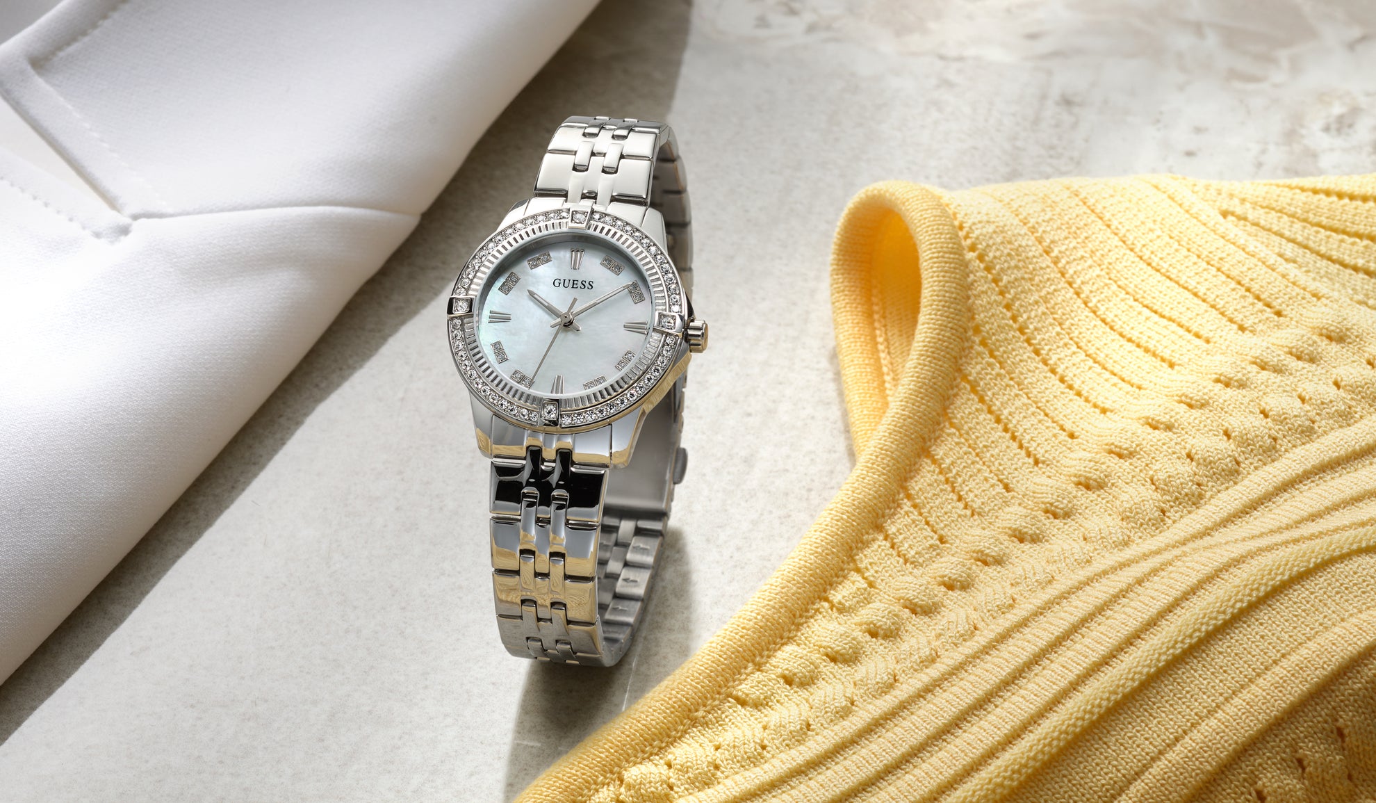 Silver watch with a white face on a light surface next to a yellow textured fabric