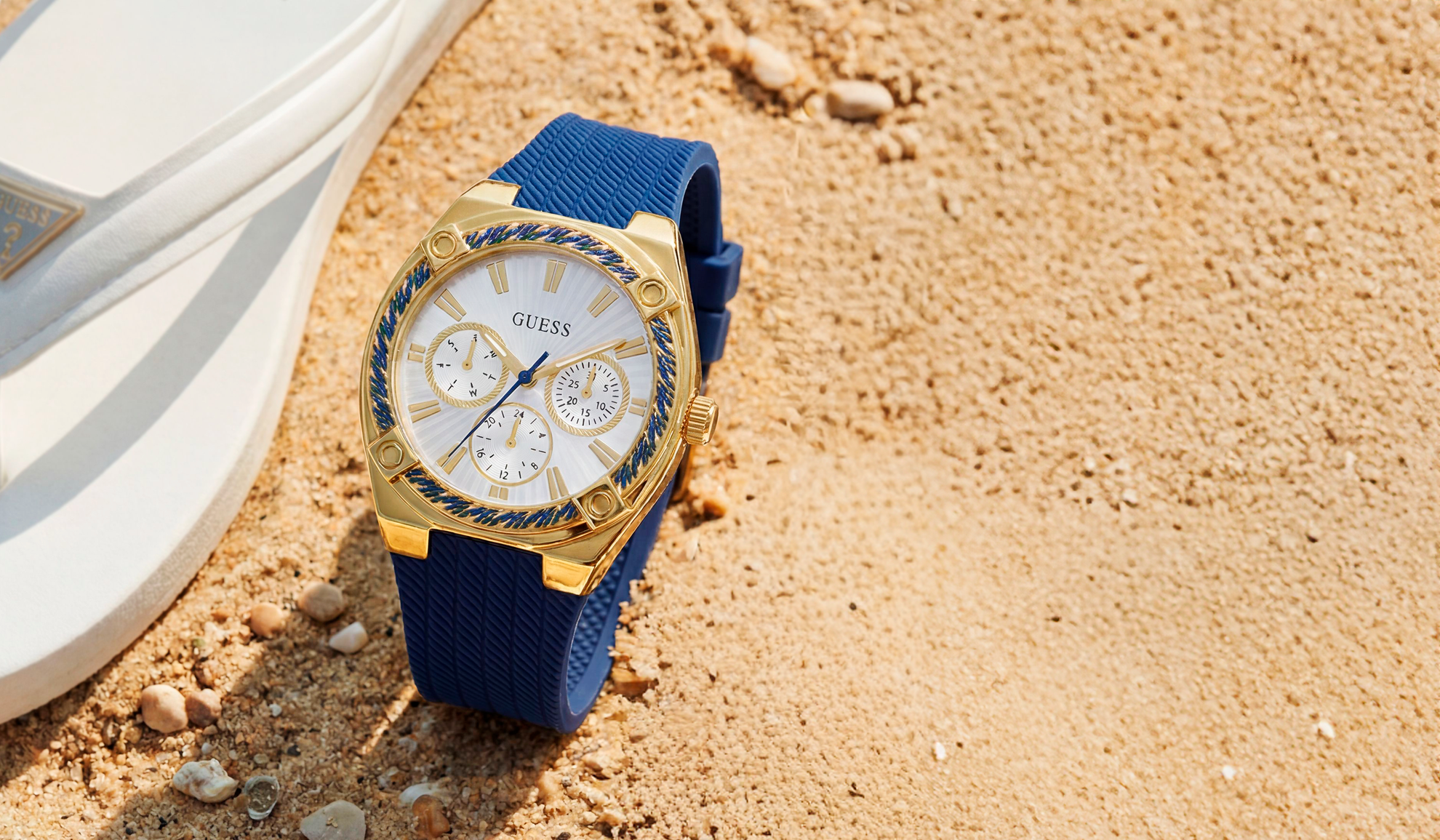 Gold watch with blue strap on sandy surface