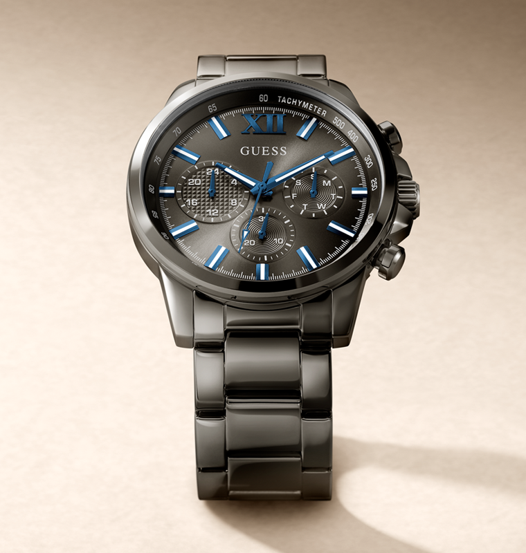 A GUESS men's chronograph watch with a dark gunmetal gray stainless steel case and link bracelet, featuring a textured dark gray dial with vibrant blue hands, markers, and subdial accents.