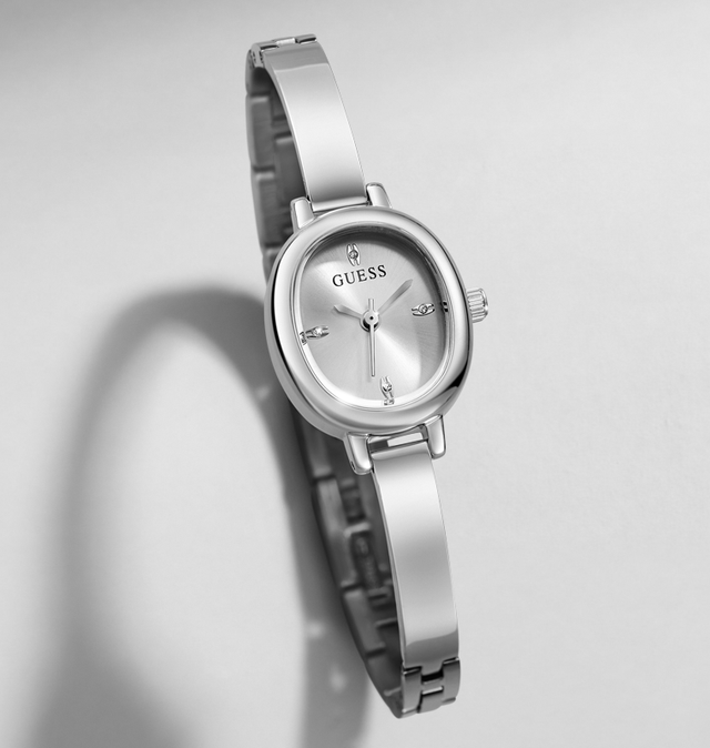 A silver-tone stainless steel wrist watch with an oval bezel, matching metal bracelet, and a silver dial featuring the GUESS brand name.