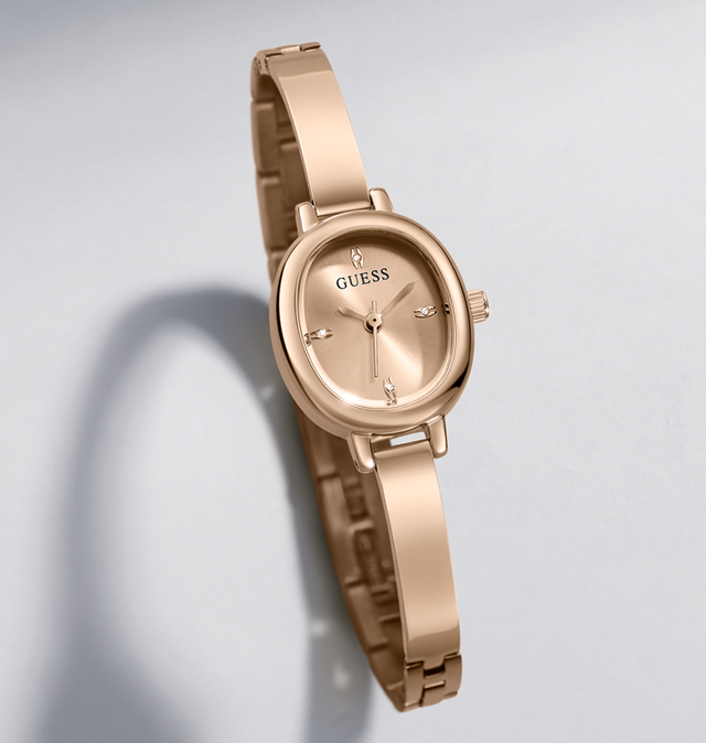 A GUESS women's watch with a rose gold-tone metal bracelet and matching oval case, displayed on a light gray background with a soft shadow.