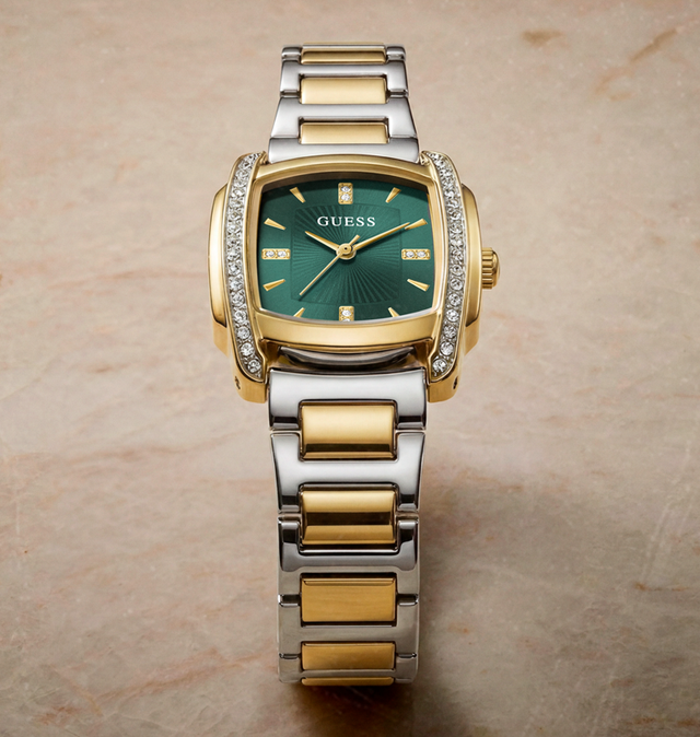 A Guess women's two-tone watch with a green dial, gold-tone case details, and a silver-and-gold link bracelet, photographed on a beige stone surface.