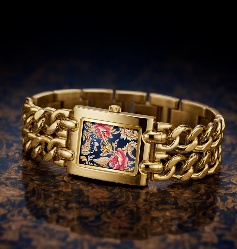 A gold-tone metal watch with a rectangular case and a highly detailed floral enamel face. The watch features a gold curb-style link bracelet and is displayed on a dark, patterned surface with a reflective finish.