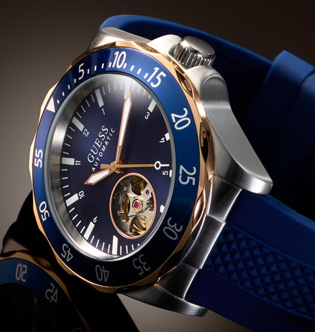 A close-up of a Guess Automatic watch with a blue dial, blue bezel, blue strap, and silver-toned case with gold-tone accents.
