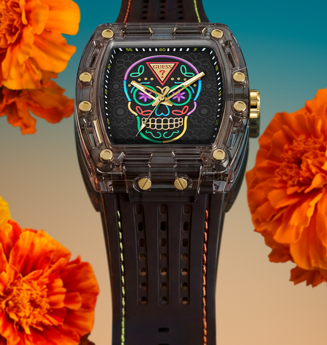 A luxury watch by GUESS with a transparent dark gray case, gold-tone screws, and a black strap. The watch face features a colorful, vibrant sugar skull graphic.