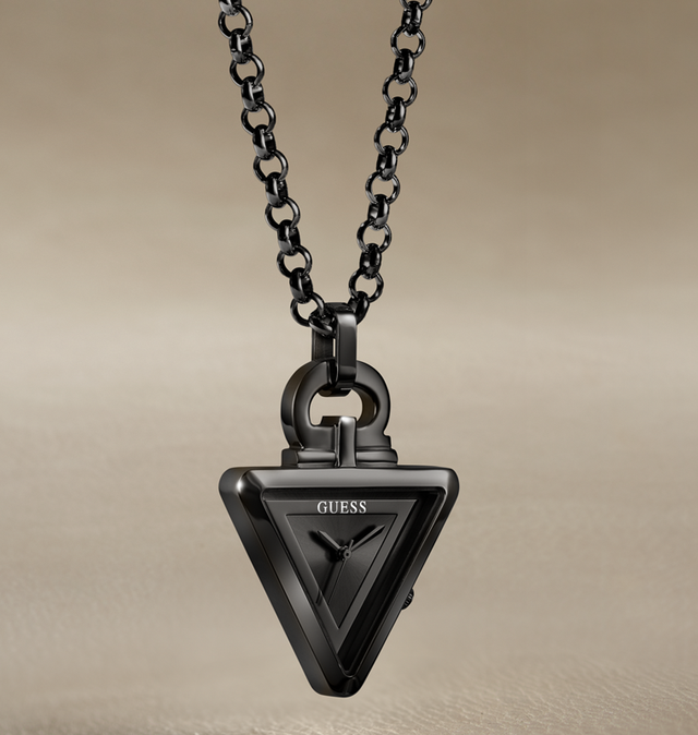A black triangular GUESS pendant necklace with a matching black link chain, shown against a warm beige gradient background.