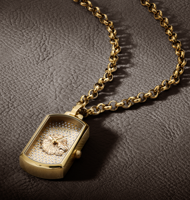 A gold-tone rectangular pendant watch with a pavé crystal face and a central rose-gold-toned emblem, hanging from a thick gold chain on a dark textured leather background.