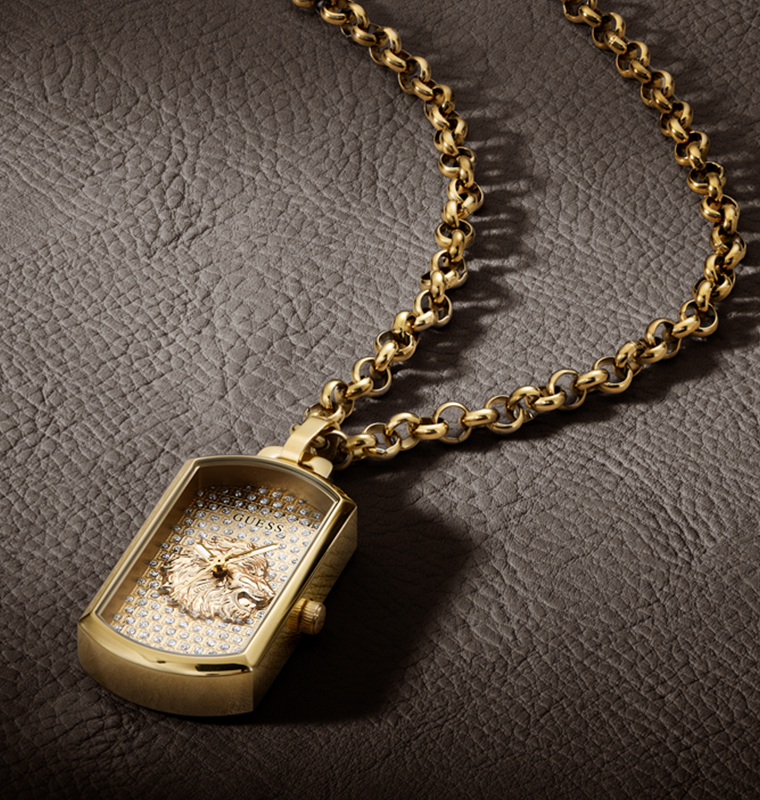 A gold-tone rectangular pendant watch with a pavé crystal face and a central rose-gold-toned emblem, hanging from a thick gold chain on a dark textured leather background.