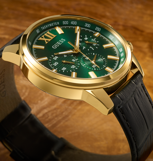 mens watch with black croco embossed leather strap, gold case and green dial at an angle on brown background