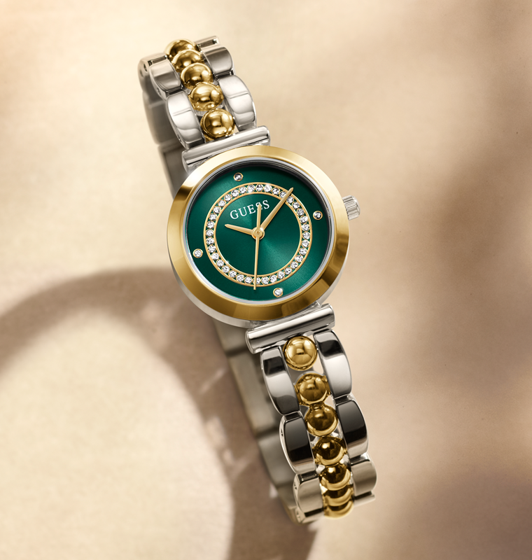 Gold and silver watch with green face on a beige background