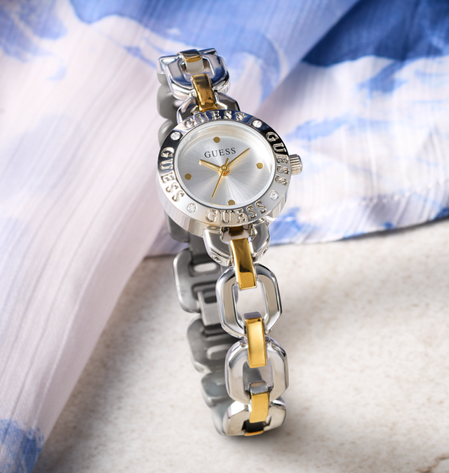 Silver and gold watch with 'Guess' branding on a light fabric background