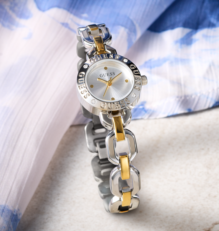 Silver and gold watch with 'Guess' branding on a light fabric background