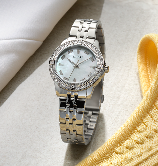 Silver Guess watch with a white face on a light surface with a yellow fabric.