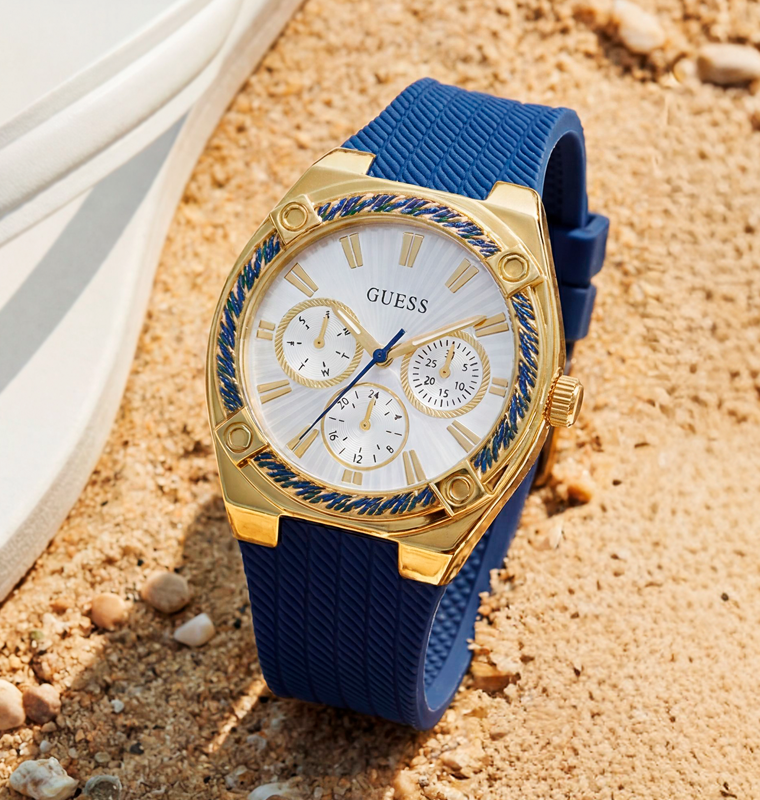 Gold and blue watch on a sandy surface with 'GUESS' branding
