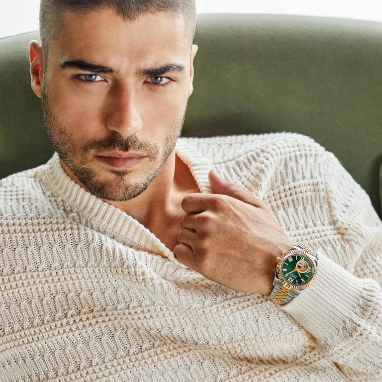Man wearing a beige sweater and a watch with a green face, sitting on a green couch.