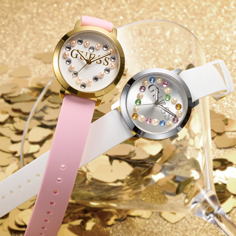 Two womens watches with pink and white straps and hearts in colored stones on the dials