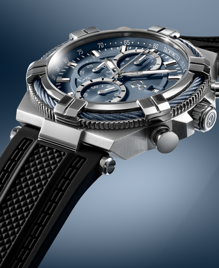 A close-up studio shot of a wristwatch with a silver-toned metal case, blue dial, and black textured strap against a blue gradient background.