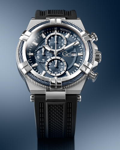 A luxury chronograph watch with a silver-tone titanium case, a dark blue dial with three subdials, and a textured black rubber strap, shown against a dark blue gradient background.