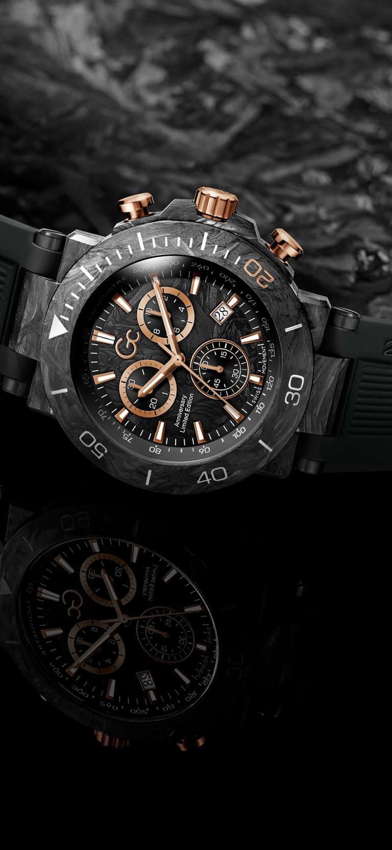 A black chronograph watch with rose gold accents and a black dial, shown against a dark textured background with a reflection below.