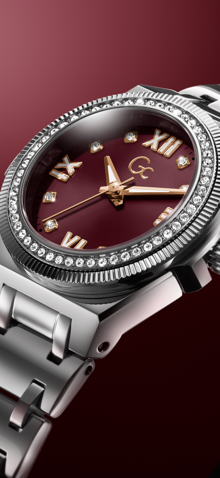 A close-up of a luxury wristwatch featuring a silver stainless steel case and bracelet, a deep burgundy dial with gold-tone Roman numerals and hands, and a bezel encrusted with clear crystals.