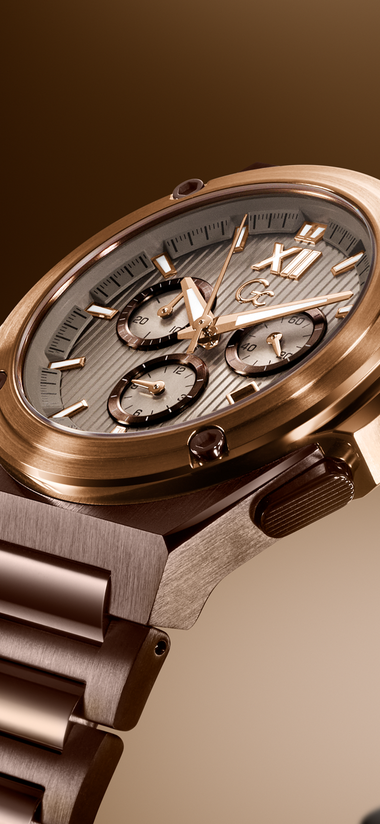 Close-up of a luxury wristwatch with a brushed rose gold-toned metal case and integrated bracelet, featuring a textured gray dial with three subdials and a warm brown gradient background.