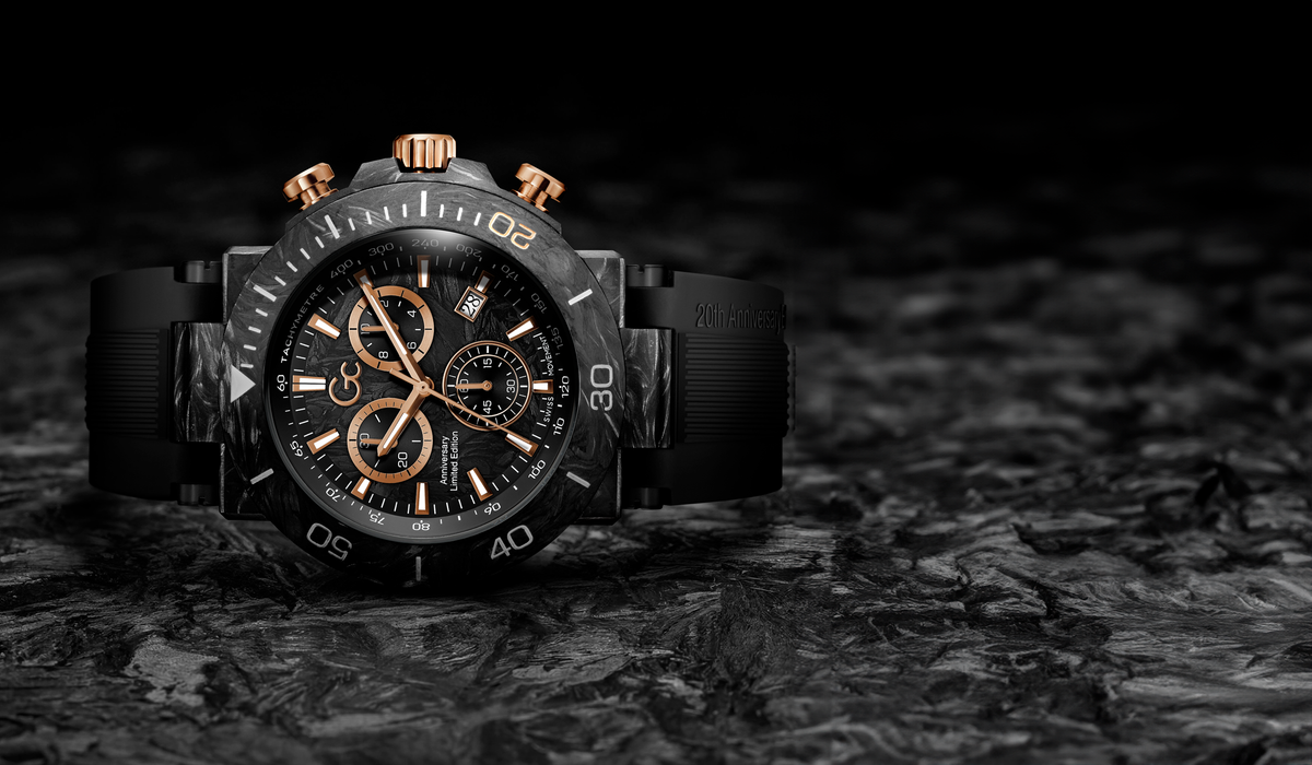 A luxury chronograph watch with a black carbon fiber case, black rubber strap, and rose gold accents on the bezel, hands, and sub-dials, set against a dark textured background.