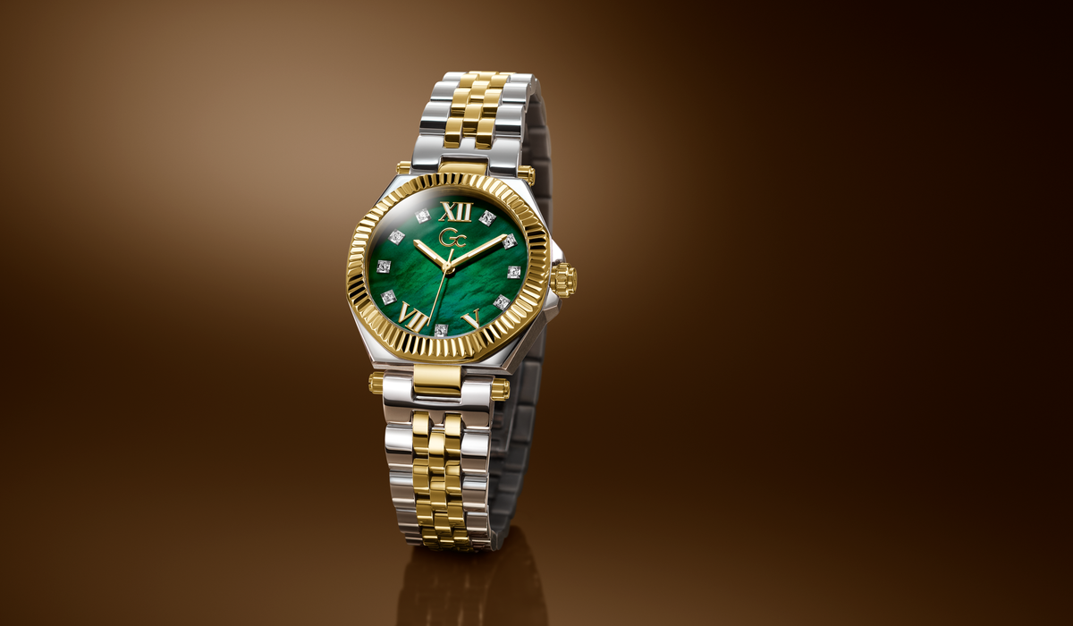 A luxury two-tone watch with a green dial, gold-tone bezel and hands, and a silver-and-gold link bracelet, shown on a dark brown gradient background.