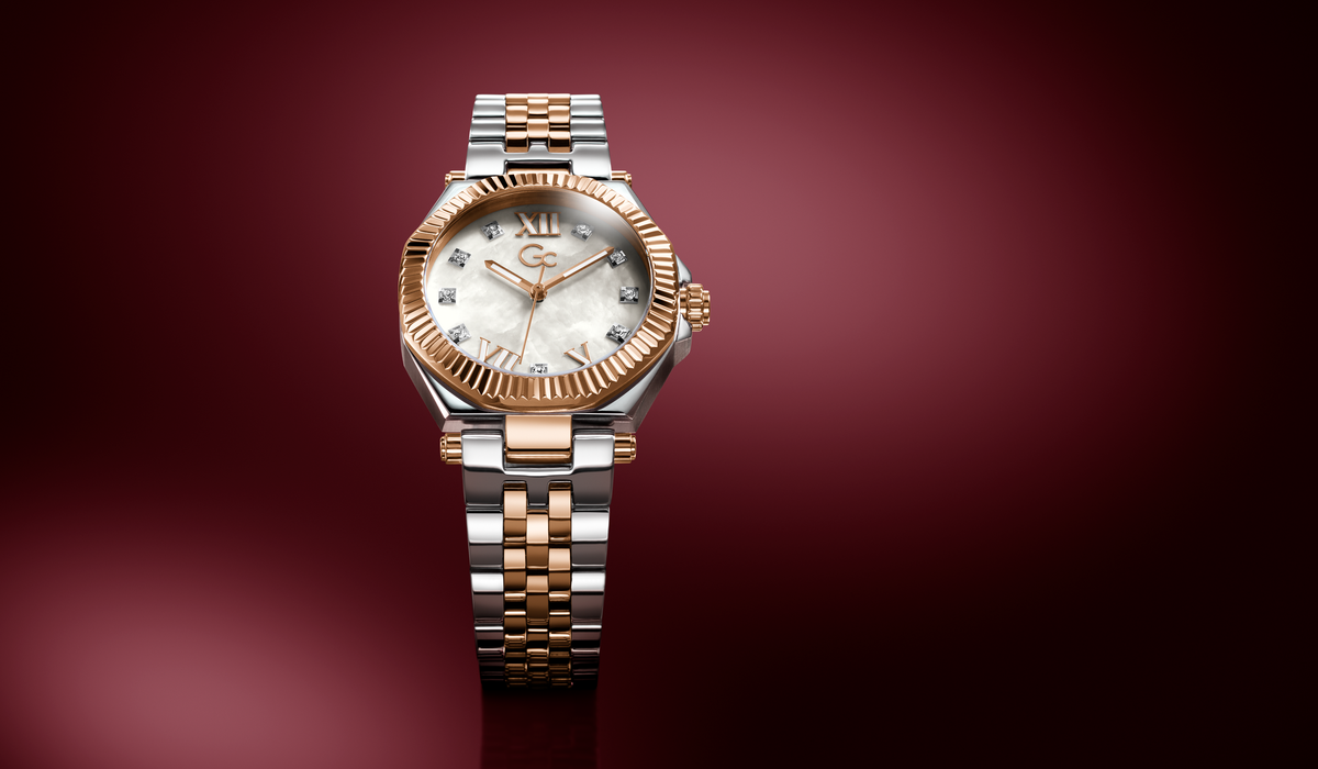 A luxury two-tone wristwatch with a silver and rose gold metal bracelet, a fluted rose gold bezel, and a white dial with diamond hour markers, set against a dark burgundy gradient background.