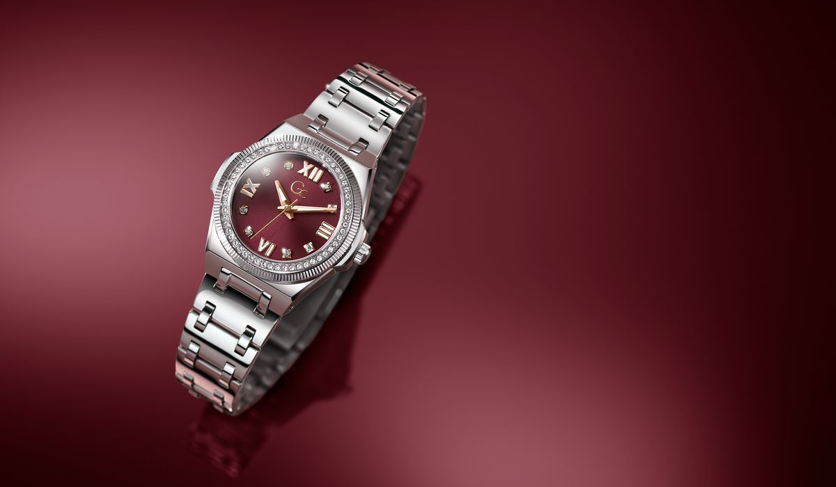 A silver-toned metal wristwatch with a dark burgundy dial and matching burgundy hour markers, shown at an angle on a reflective dark red background.