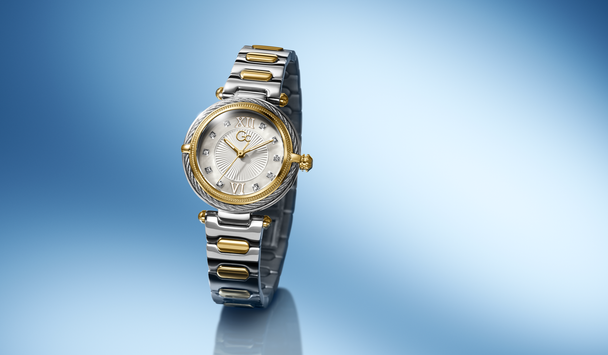Gc Vogue Cable Mini Small Size Metal watch with gold and silver band on a gradient blue background