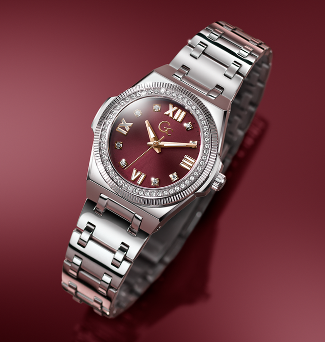 A luxury women's watch featuring a silver stainless steel bracelet, a bezel set with small clear crystals, and a deep burgundy dial with gold-tone Roman numerals and hands.