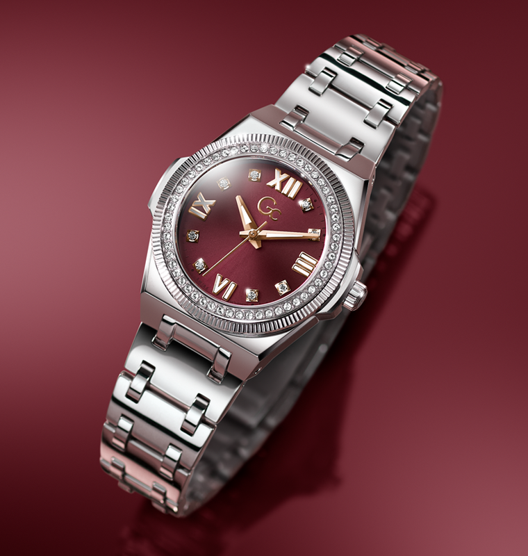 A luxury women's watch featuring a silver stainless steel bracelet, a bezel set with small clear crystals, and a deep burgundy dial with gold-tone Roman numerals and hands.