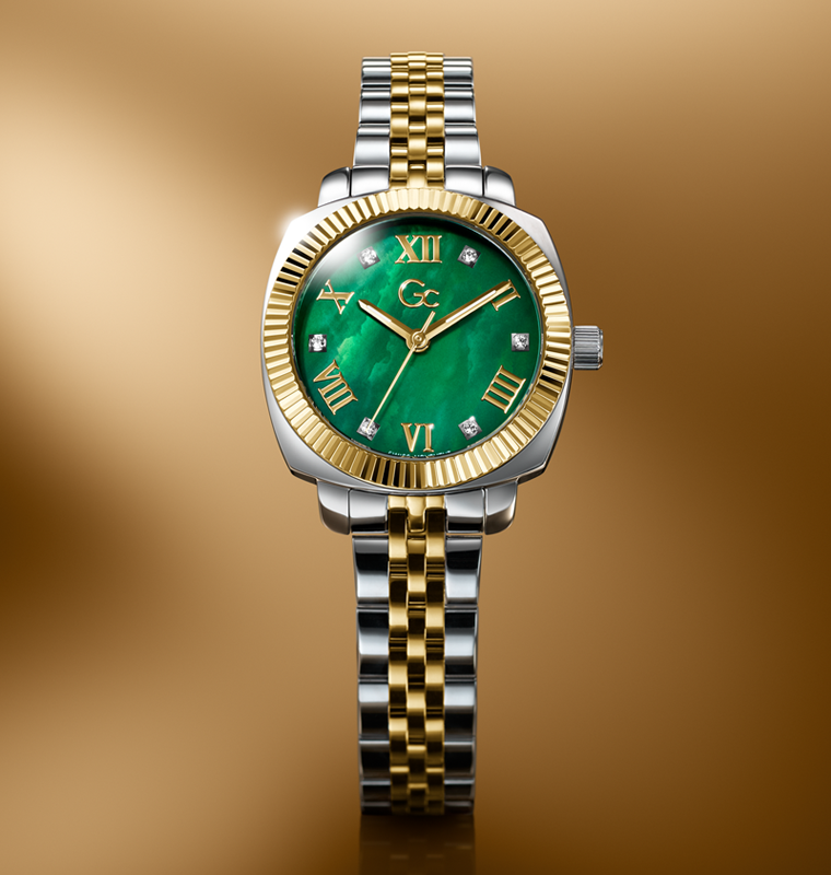 Luxury watch with green face and gold and silver band on a gold background
