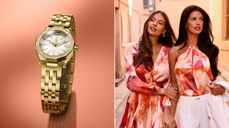 Gold Gc watch on a gradient background with two women in colorful outfits walking together.