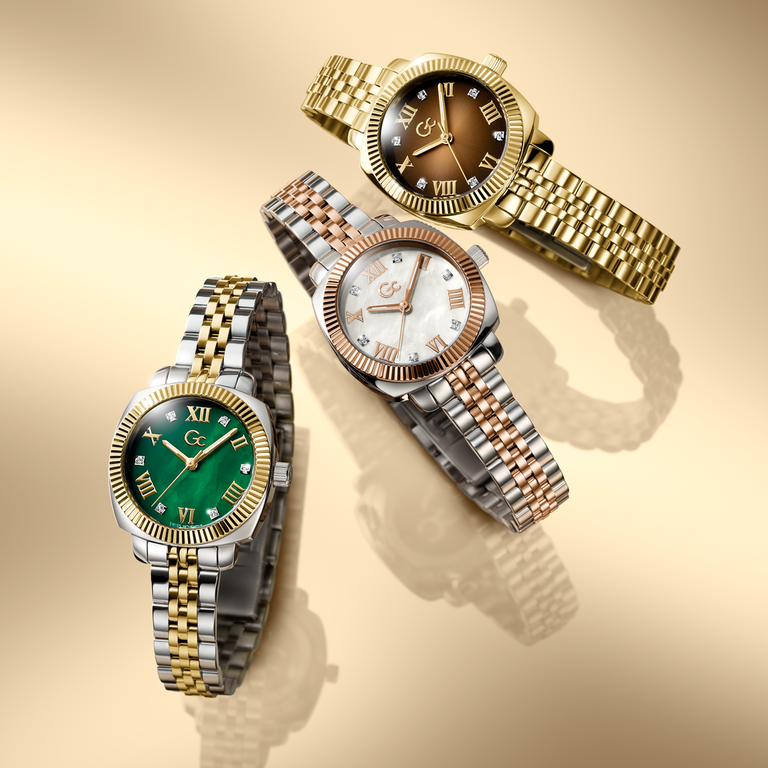 Three elegant Gc wristwatches with different colored faces on a beige background