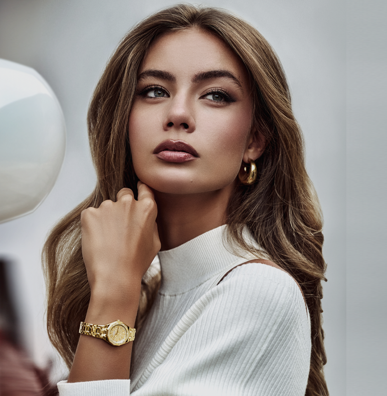 Woman wearing a gold watch and earrings against a neutral background