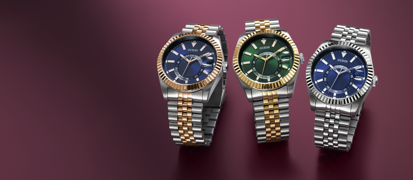 Three watches with different colored faces and metal bands on a maroon background