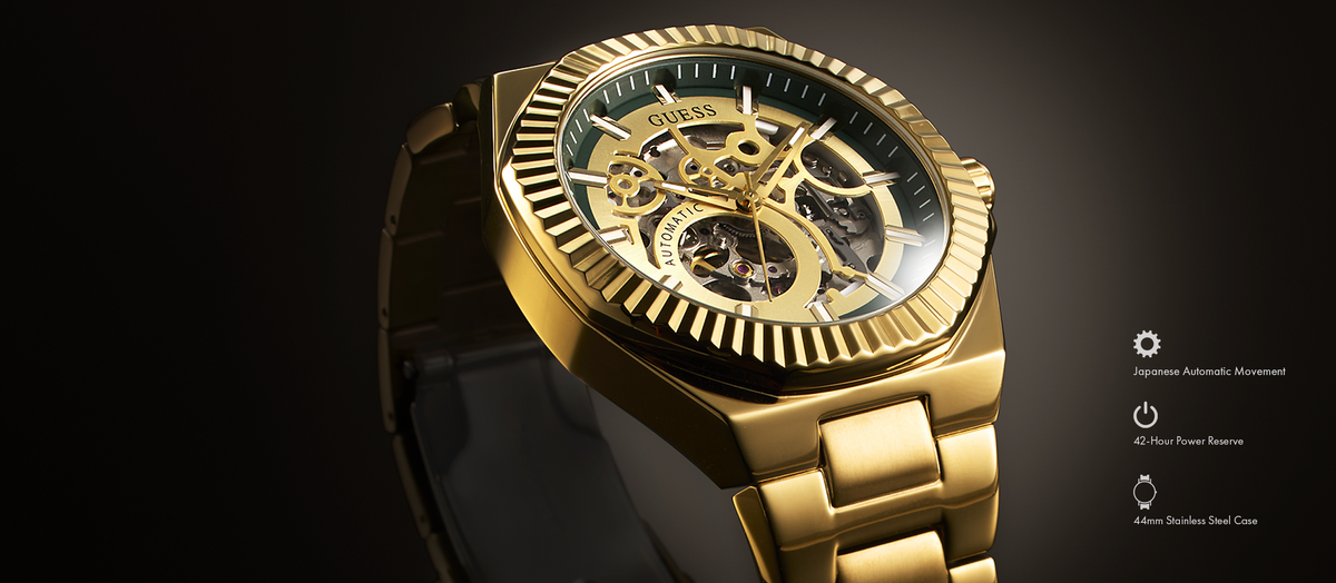 A luxury gold-tone skeleton watch with a black strap, shown at a three-quarter angle on a dark gradient background. The watch features a detailed gold-tone dial with visible mechanical gears and a fluted bezel.