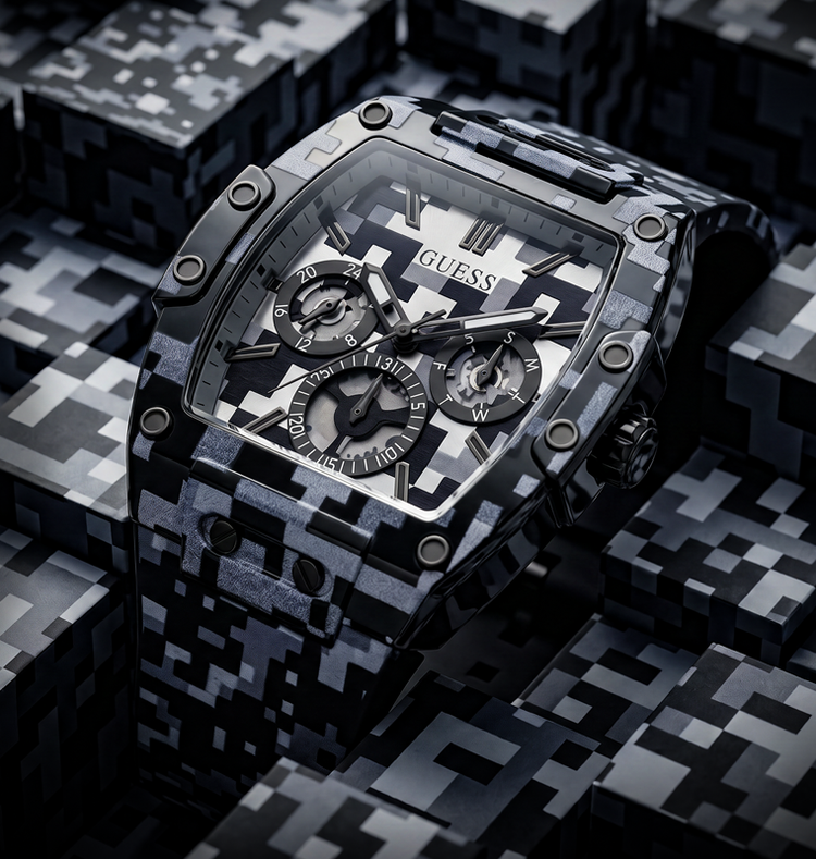 A Guess wristwatch with a black and white pixelated/digital camouflage patterned case and matching dial details, resting on a dark gray and black pixelated surface.