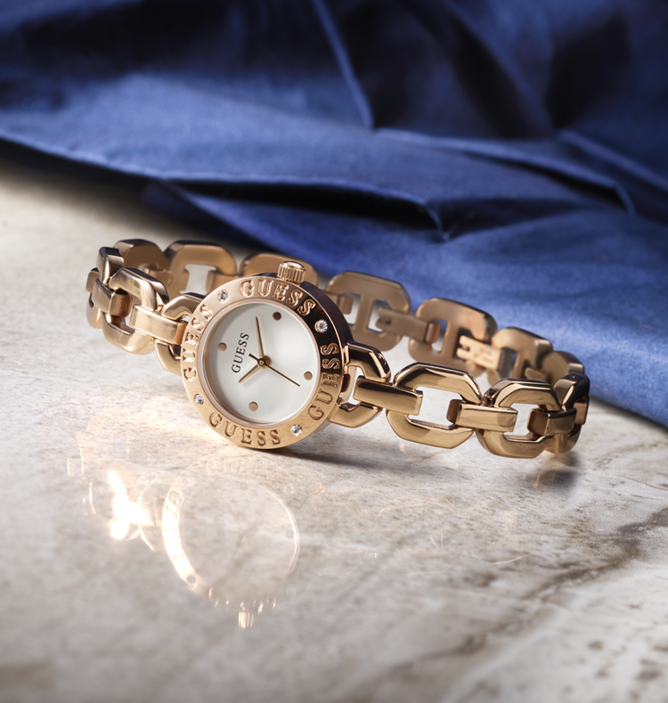 Rose Gold chain-link watch on a reflective surface with a blue fabric background