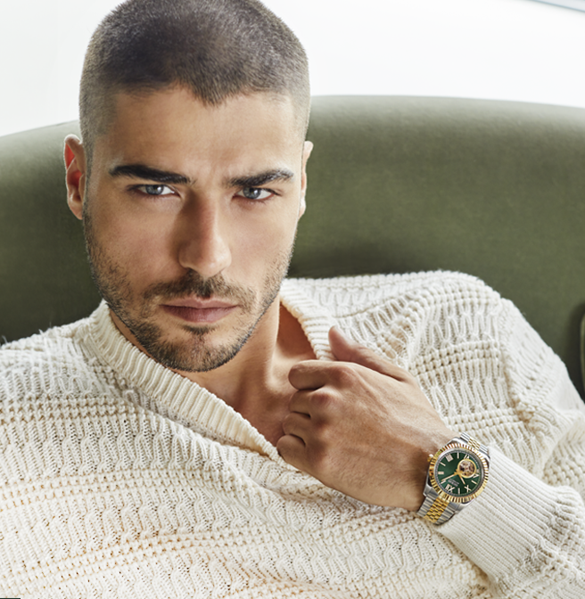Man wearing a cream sweater and gold GUESS watch with a green dial, sitting on a green couch.