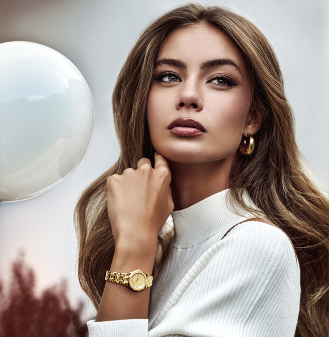 Woman wearing a gold GUESS watch and earrings with a blurred background