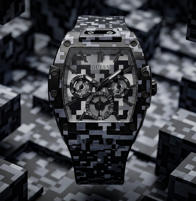 A Guess wristwatch with a black and gray digital camouflage pattern on the case and strap, shown against a dark, geometric background.