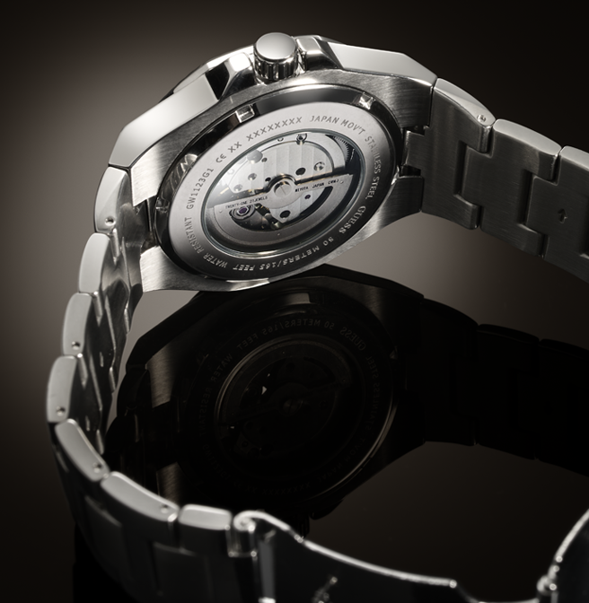 Close-up of a stainless steel wristwatch showing the back case with a transparent window revealing the mechanical movement, attached to a matching metal link bracelet on a dark reflective surface.