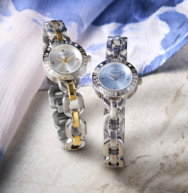 Two Guess watches with chain-like bracelets on a marble surface.